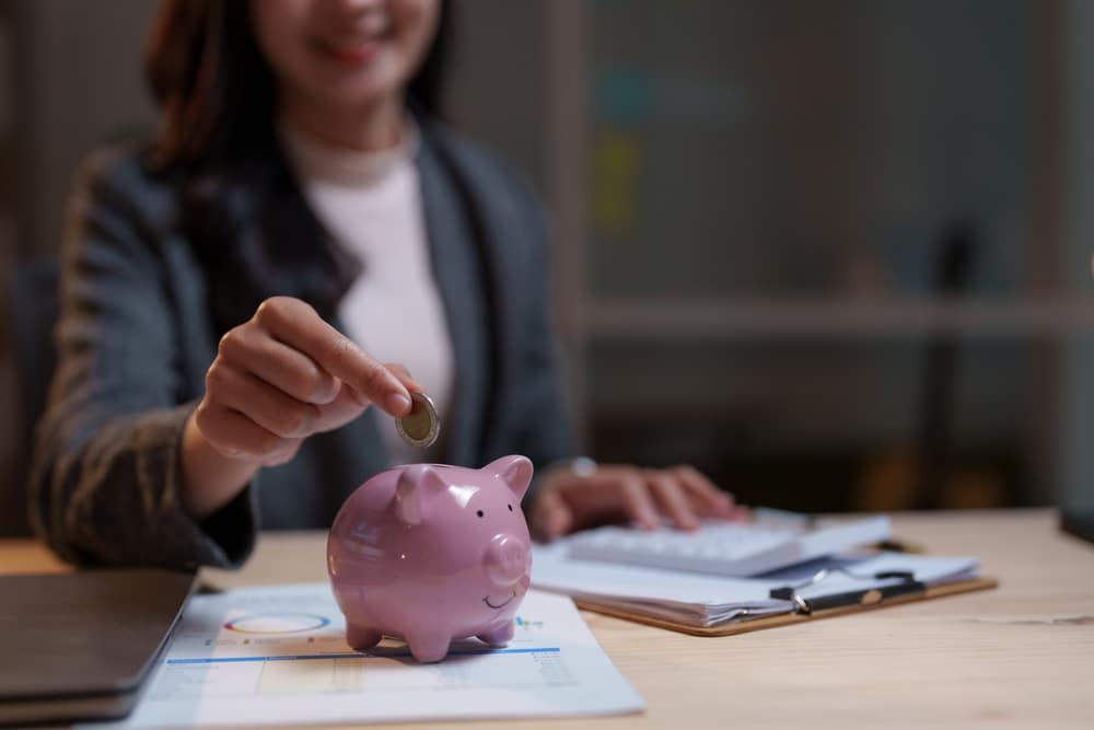 Smiling,Businesswoman,Putting,Coin,Into,Piggy,Bank,,Calculating,Financial,Savings